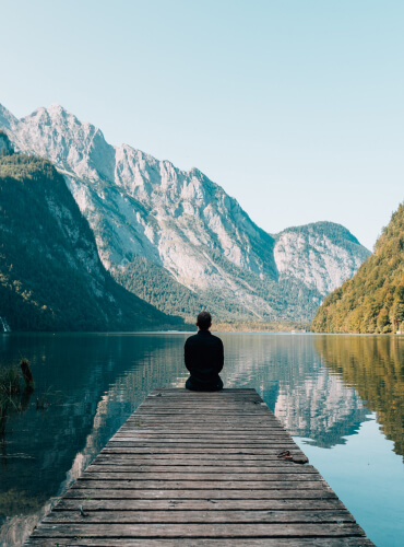 Man Sitting at end of quay looking at water and moutains